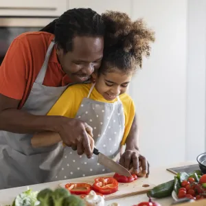 Cooking With Dad. Happy Black Girl Preparing Lunch With Father In Kitchen Together, Caring African American Daddy Making Vegetable Meal With His Preteen Female Child While They Bonding At Home